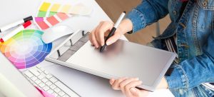 young woman artist in jeans jacket drawing something on graphic tablet at the office